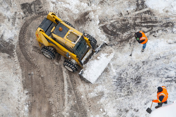 Top view of a snow-removing machine and workers in orange uniforms on a dirty road