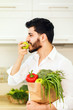 © proimagecontent - Black-haired bearded man, in smart white shirt, holding shopping pack with fresh, organic food and green apple inthe kitchen