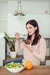 © Iulia - Smiling young woman in the kitchen near desk and eats cereals. Healthy life concept