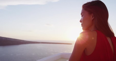 Fototapete - Beautiful woman enjoying the beautiful view of Aegean Sea during sunset. Female tourist is wearing red dress while standing at caldera. She is on her vacation in Santorini.