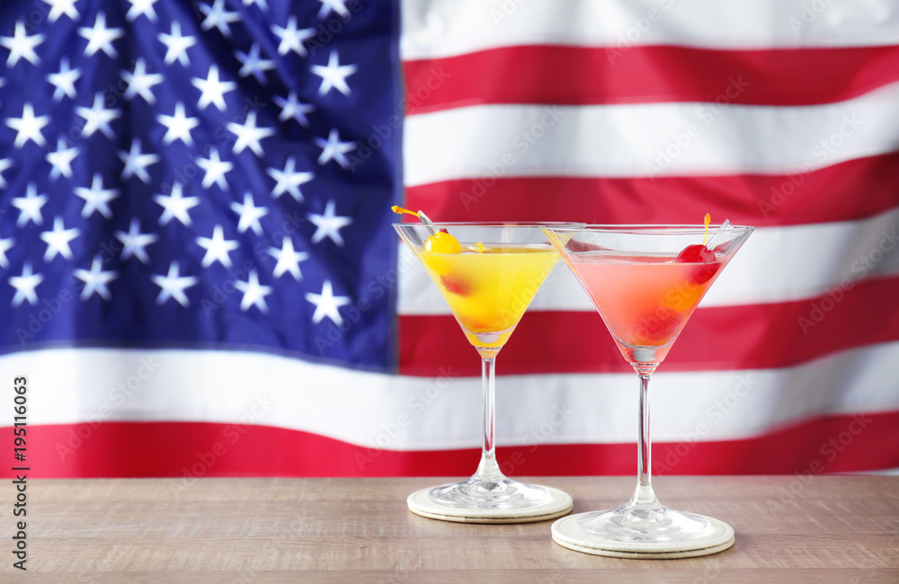 Glasses with alcoholic cocktails on table against American flag background