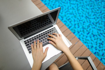 Wall Mural - view from above of woman hands pressing buttons on laptop at sunny day swimming pool. concept of business freelance working, new technologies. Fingers typing on the computer keyboard