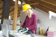 © epiximages - young, pretty, blonde woman with yellow helmet and green gloves is planning on the notebook and tablet the expansion of her loft