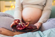 Closeup of pregnant woman's belly and pomegranate