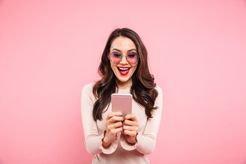 Wall Mural - Pleased woman with red lips chatting or using internet on mobile phone, over pink background