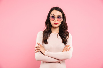 Wall Mural - Photo of adult girl with brooding look and hands crossed looking on camera expressing resentment, isolated over pink background