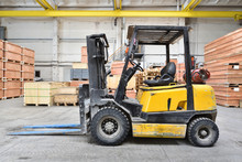 The Forklift Is Old And Scratched In A Large And Light Warehouse. Yellow Color