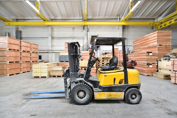 The forklift is old and scratched in a large and light warehouse. Yellow color