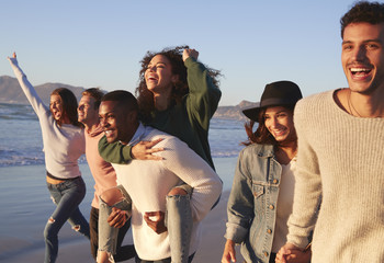 Group Of Friends Having Fun Running Along Winter Beach Together