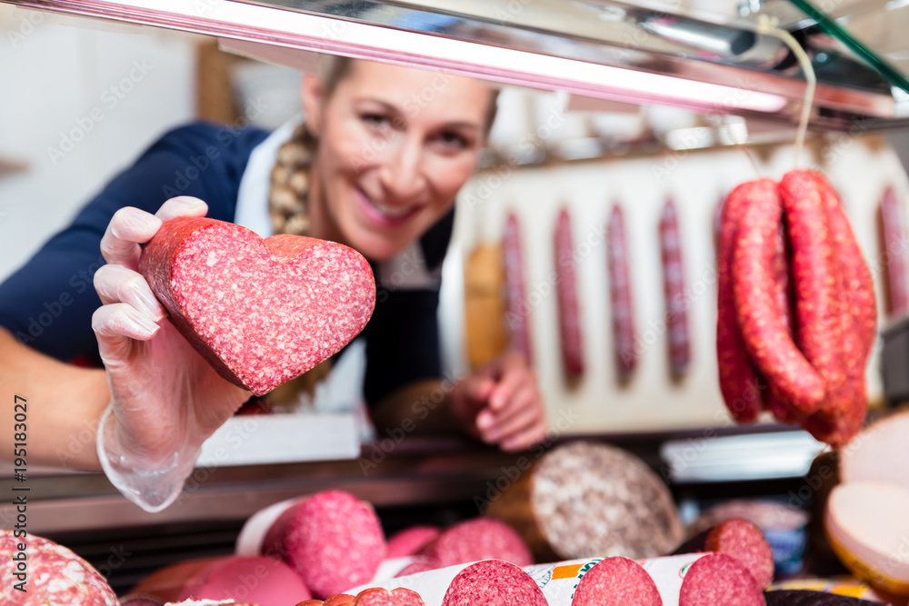 Sales woman in meat shop showing a heart shaped sausage to customer