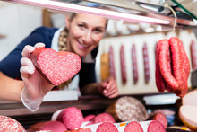 Sales Woman In Meat Shop Showing A Heart Shaped Sausage To Customer