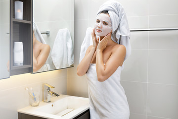 Wall Mural - Woman in bathroom is applying facial sheet mask