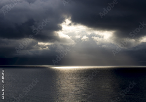 Fotografie, Obraz Sun Breaks Through Dark Clouds Over Ocean