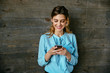Cheerful beautiful businesswoman using a mobile phone, looking at screen. Dressed in elegant blouse