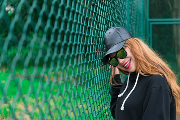 Wall Mural - Cool Hipsters girl in black hood with black hat and black sunglass,lifestyle of teenage,thailand people,young woman posing on fence