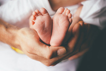 small feet of a newborn supported by the hand of his father