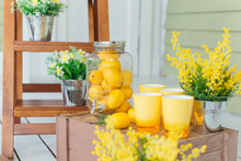 The Glass Jar Is Completely Filled With Lemons And Beside It There Are Yellow Glasses On A Wooden Table. Design Concept.