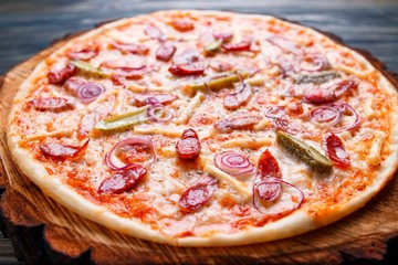 Hot pizza with salami, onions and gherkins served on chopped wood. Italian food, restaurant menu concept