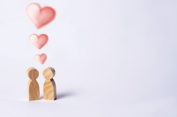 Two wooden figures of people stand together on a white background with hearts over their heads. Concept of love, couple, young people. Minimalism. Romance, a meeting, a novel.
