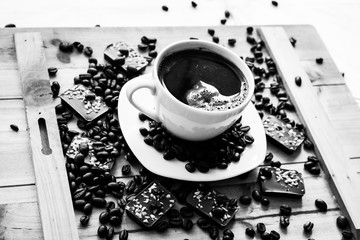 Single white cup with black coffee on wooden table with beans and almond chocolate black and white photography