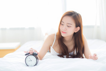 Wall Mural - Beautiful asian young woman turn off alarm clock in morning, wake up for sleep with alarm clock, relax and lifestyle concept.