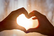 © SecondSide - Female hands in the form of heart against the window pass sun beams. Hands in shape of love heart silhouetted against the sun