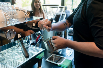 High angle view close-up of the hand of a barista holding a stainless mug while using a modern coffee machine