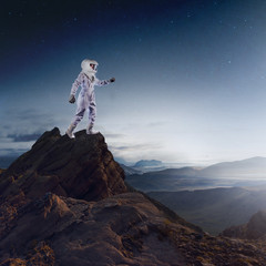 Wall Mural - Portrait of astronaut in a space suit. Futuristic astronaut on the planet, standing on top of a mountain and stretches his hand away