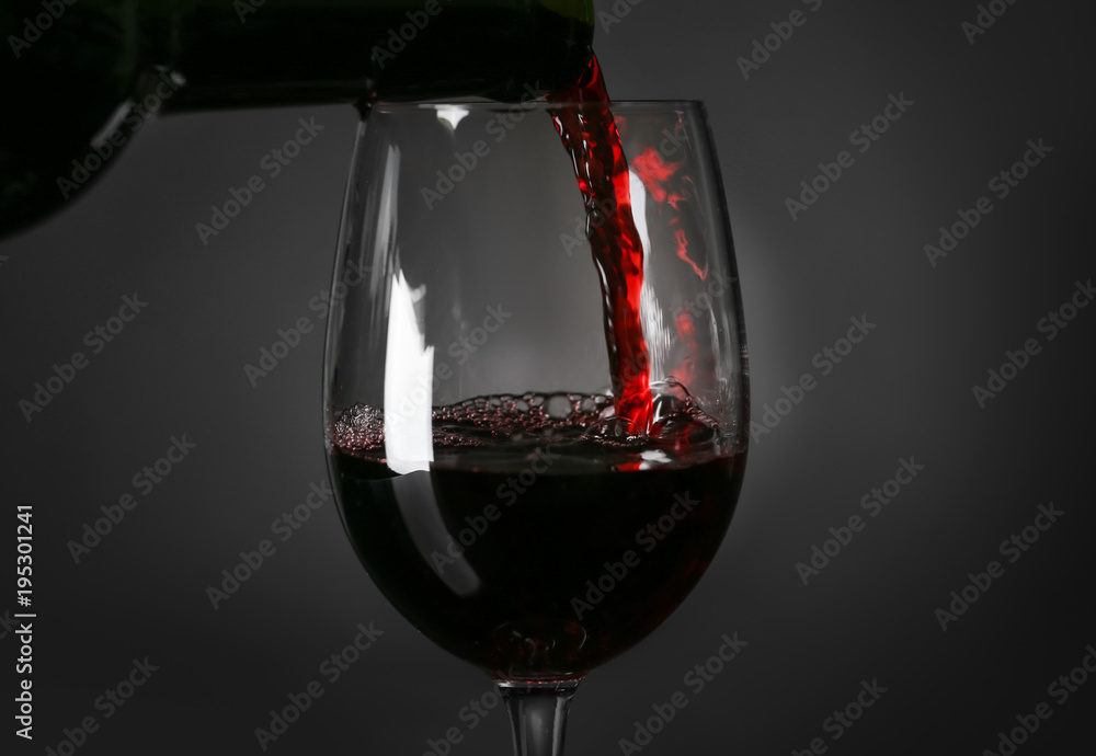Pouring red wine into glass on black background, closeup
