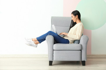 Young Asian woman using laptop in armchair, indoors