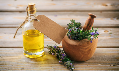 Wall Mural - Rosemary essential oil and fresh blooming twig in a mortar, wooden table, blank tag, copy space