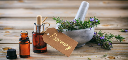 Wall Mural - Rosemary essential oil and fresh blooming twig in a mortar, wooden table, tag with text rosemary