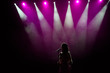 © nagaets - Girl in long gown performing on stage. Girl singing on the stage in front of the lights. Silhouette of singer standing on stage at microphone.