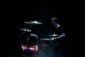 music, people, musical instruments and entertainment concept - male musician with drumsticks playing drums on the stage.