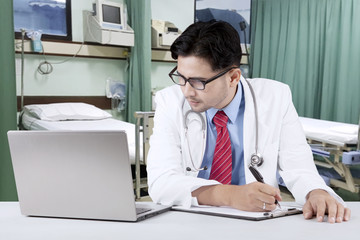 Canvas Print - Doctor looking at his laptop while writing a prescription