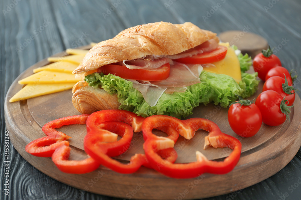 Wooden board with tasty croissant sandwich on table