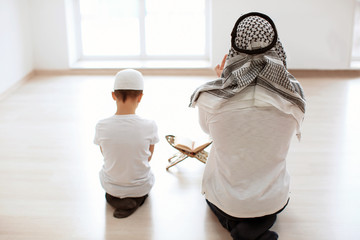 Wall Mural - Muslim father and son praying together, indoors