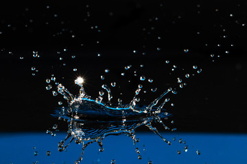 Wall Mural - drop of water liquid with splash isolated. the drop explodes in the water sending spray to the sides and circle ripples around it. the water is blue