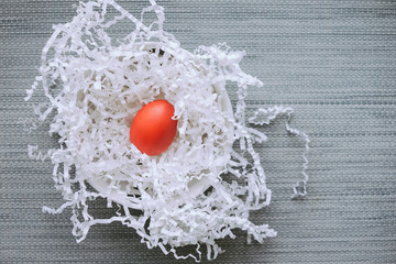 Wooden red easter egg in a bowl nest on a gray background with paper slips. View from above.