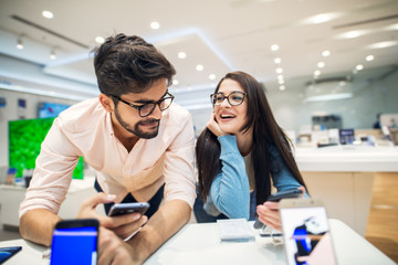 Canvas Print - Young satisfied stylish charming couple testing the new model of a mobile from the desk in the tech store.