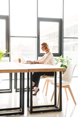 Happy young business woman sitting in office using laptop