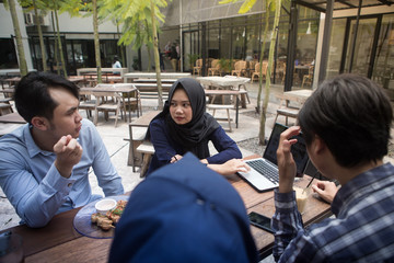 Small Creative Team of South East Asian Young People Looking at a Laptop. Having Meeting and Discussion at Outdoors Cafe.