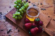Honey In Jar With Strawberries And Green Grapes On Wooden Plate