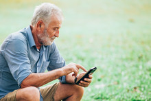 Senior Men Using A Smartphone While Sitting On Grass In The Park