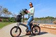 A smiling woman with electric bicycle in the park Holds a helmet