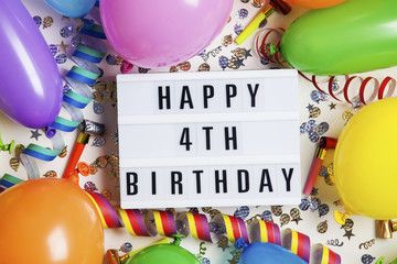 Happy 4th birthday celebration message on a lightbox with balloons and confetti