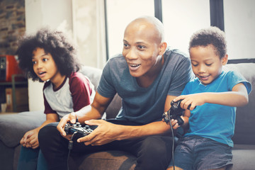 african american family at home sitting in sofa couch and playing console video games together.