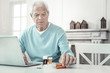 © Viacheslav Yakobchuk - Serious illness. Deep aged sad man sitting in the room by the table using the laptop and overlooking pills.