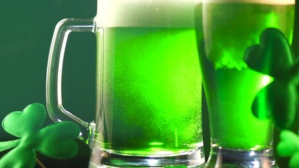 Wall Mural - St. Patric's Day green beer pouring over deep green background, decorated with shamrock leaves. Pint of green beer closeup. 4K UHD video footage. 3840X2160