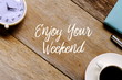 © MohamadFaizal - Top view of a cup of coffee,clock,notebook and pen on wooden background written with ENJOY YOUR WEEKEND.